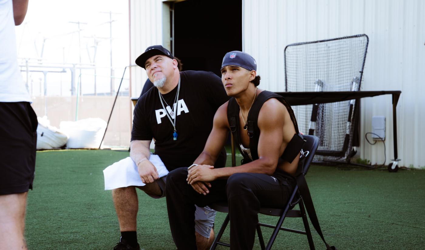 A Pro Vision coach and a quarterback watch practice from the sideline