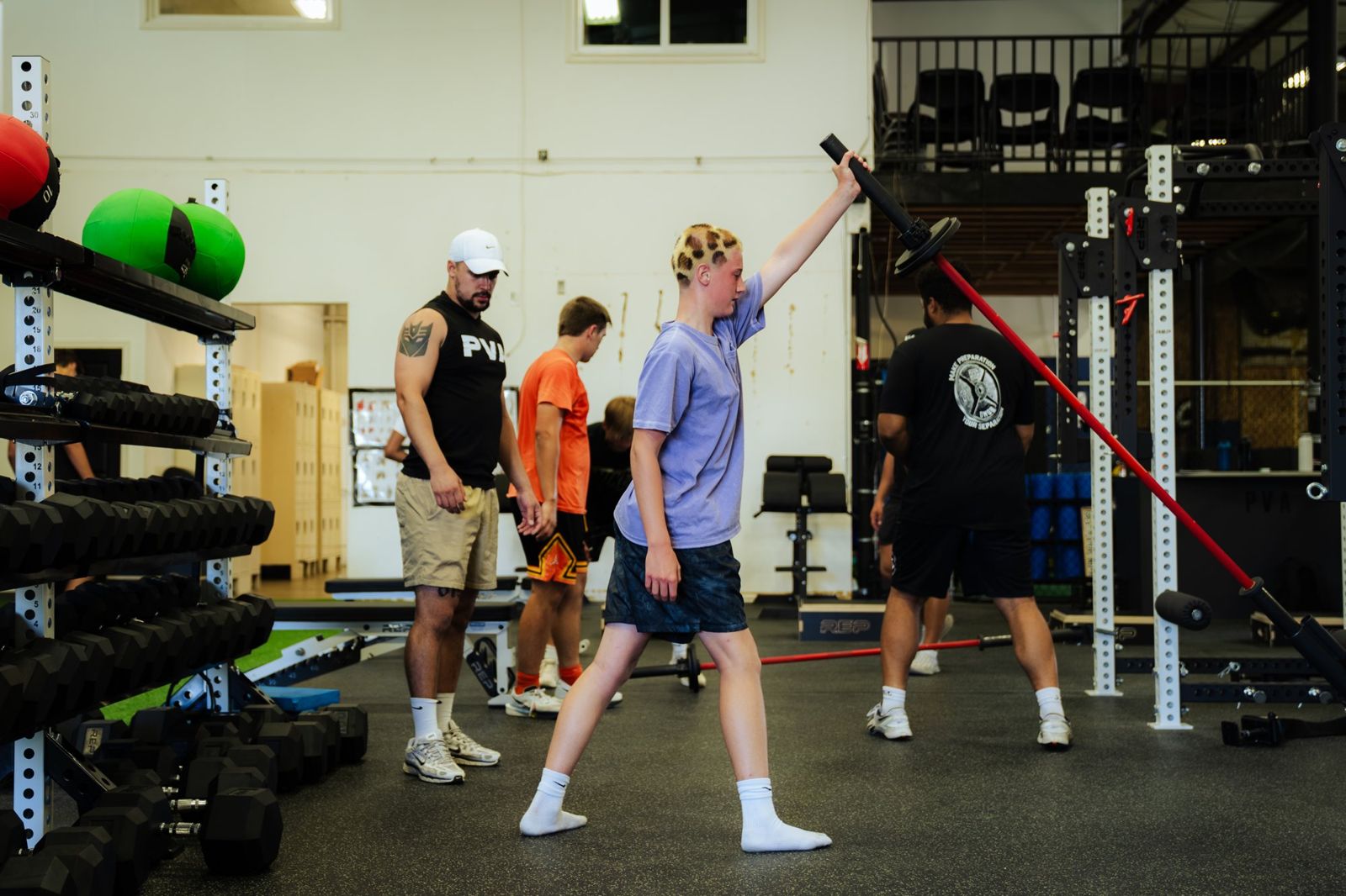 A coach watches an athlete work through a landmine press in the weight room