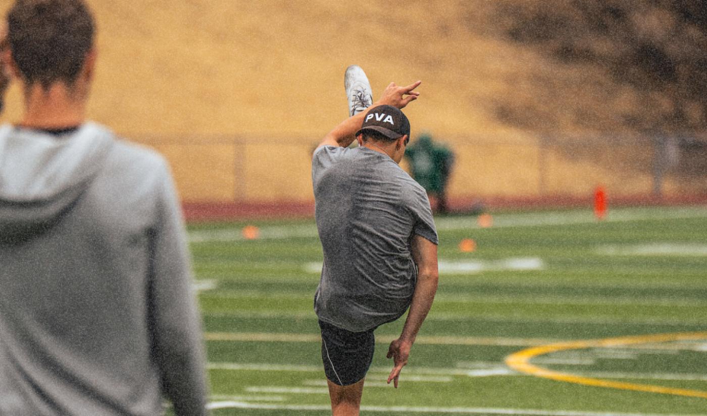 A kicker follows through on a field goal while a coach watches